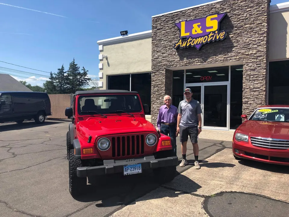 Visitors beside a red Jeep outside L & S Automotive